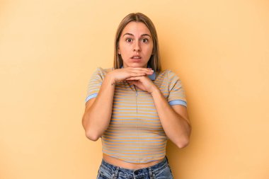 Beyaz tenli genç bir kadın sarı arka planda izole edilmiş şans diliyor, şaşırmış ve ağzını açıp önüne bakıyor..