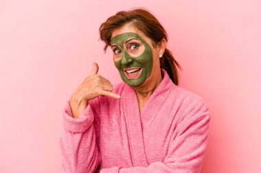 Middle age caucasian woman wearing a facial mask isolated on pink background showing a mobile phone call gesture with fingers.