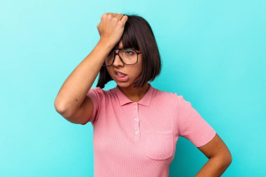 Mavi arka planda izole edilmiş genç bir ırk kadını bir şeyi unutuyor, alnına avuç içi ile vuruyor ve gözlerini kapıyor..