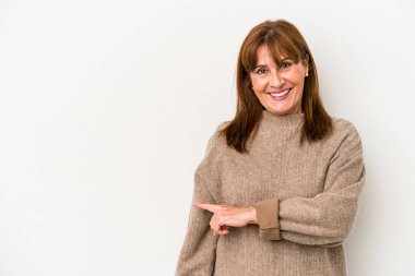 Beyaz arka planda izole edilmiş orta yaşlı beyaz bir kadın gülümsüyor ve boş alanda bir şeyler gösteriyor..