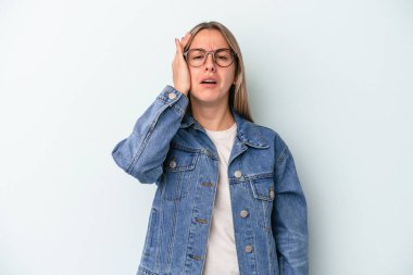 Mavi arka planda izole edilmiş genç beyaz kadın yorgun ve uykulu ellerini başının üstünde tutuyor..