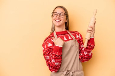 Genç fırıncı kadın Noel için kurabiye yapıyor sarı arka planda izole edilmiş başparmak uzakta, gülüyor ve kaygısız.