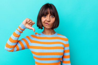 Mavi arka planda izole edilmiş genç melez kadın baş parmağını aşağı gösteriyor, hayal kırıklığı konsepti..