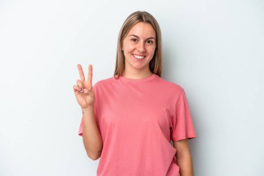 Mavi arka planda izole edilmiş genç beyaz kadın zafer işareti gösteriyor ve gülümsüyor..