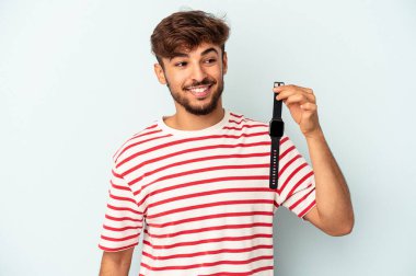 Mavi arka planda izole edilmiş bir kol saati tutan genç melez adam gülümsüyor, neşeli ve keyifli görünüyor..