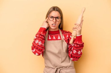 Sarı arka planda izole edilmiş, Noel için kurabiye yapan genç fırıncı kadın işaret parmağıyla yaptığı hayal kırıklığı jestini gösteriyor..