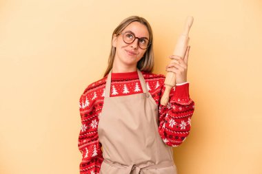 Genç fırıncı kadın Noel için kurabiye yapıyor sarı arka planda izole edilmiş hedeflere ve amaçlara ulaşma hayali kuruyor.