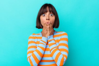 Mavi arka planda izole edilmiş genç bir ırk kadını şok olmuş, ağzı ellerle kaplanmış, yeni bir şey keşfetmeye hevesli..