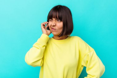Young mixed race woman isolated on blue background covering ears with fingers, stressed and desperate by a loudly ambient. clipart