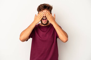 Gri arka planda soyutlanmış genç bir ırk. Gözleri ellerle kaplıyor. Gülümsüyor ve bir sürpriz bekliyor..