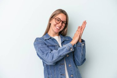 Mavi arka planda izole edilmiş genç beyaz kadın enerjik ve rahat hissediyor, ellerini ovuşturuyor..