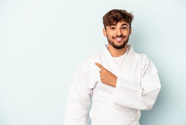 Mavi arka planda karate yapan genç melez adam gülümsüyor ve boş alanda bir şeyler gösteriyor..