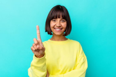Mavi arka planda izole edilmiş genç melez kadın bir numarayı parmağıyla gösteriyor..