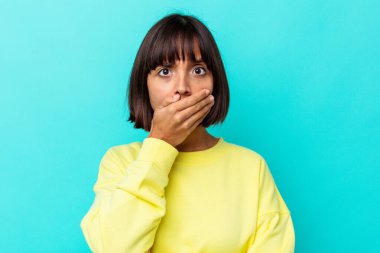 Mavi arka planda izole edilmiş genç melez kadın elleri endişeli bir şekilde ağzı örtüyor..