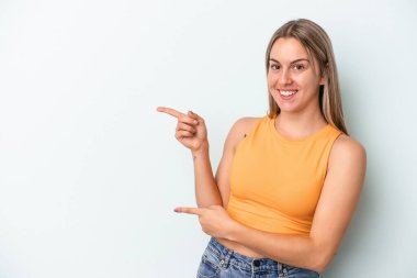 Mavi arka planda izole edilmiş genç beyaz kadın işaret parmağıyla işaret ederek heyecanlanıyor..