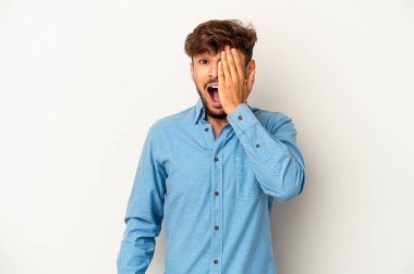 Genç melez adam gri arka planda izole edilmiş. Yüzünün yarısını avuç içiyle kaplayarak eğleniyor..