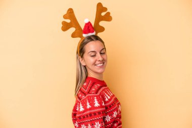 Sarı arka planda izole edilmiş bir Noel geyiği şapkası takan beyaz bir kadın gülümsüyor, neşeli ve keyifli görünüyor..