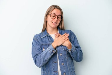 Mavi arka planda izole edilmiş beyaz bir kadın, dost canlısı bir ifadeye sahip, avuçlarını göğsüne bastırıyor. Aşk konsepti.
