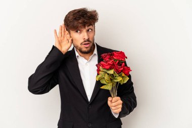 Young mixed race man holding bouquet of roses isolated on white background trying to listening a gossip.