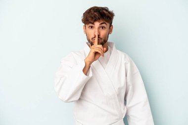 Young mixed race man doing karate isolated on blue background keeping a secret or asking for silence.