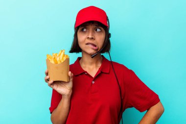 Genç, melez, fast food restoranı çalışanı elinde patates kızartması tutan, mavi arka planda kafası karışık, kuşkulu ve güvensiz bir kadın..