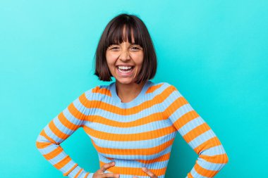 Genç melez kadın mavi arka planda izole edilmiş. Kendine güvenen, ellerini kalçasında tutan..