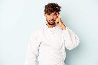 Young mixed race man doing karate isolated on blue background pointing temple with finger, thinking, focused on a task.