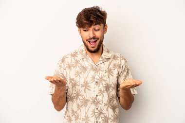 Genç melez adam gri arka planda izole edilmiş. Elinde avuç içi olan bir şeyle kameraya sunuyor..