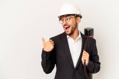 Young mixed race architect man wearing a helmet isolated on grey background points with thumb finger away, laughing and carefree.