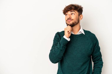 Genç melez adam gri arka planda izole edilmiş şüpheli ve şüpheci bir ifadeyle yana bakıyor..