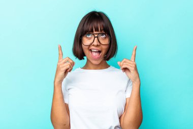 Mavi arka planda izole edilmiş genç melez kadın iki parmağı da boş bir alan gösteriyor..