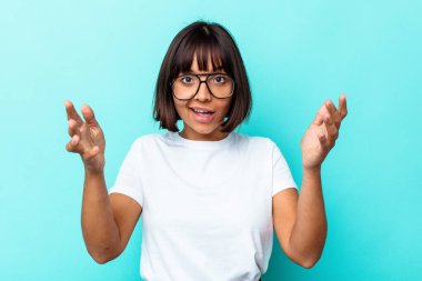 Mavi arka planda izole edilmiş genç melez kadın zaferi ya da başarıyı kutluyor, şaşırıyor ve şok oluyor..