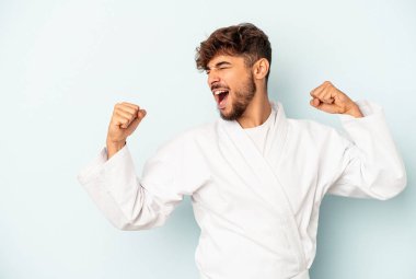 Mavi arka planda karate yapan genç melez bir adam zaferden sonra yumruğunu kaldırıyor, kazanan konsept..