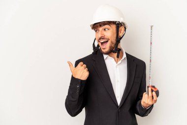 Miğfer takan ve taksimetre tutan genç bir mimar. Gri arka plan noktalarına izole edilmiş, baş parmak uzakta, gülen ve kaygısız..