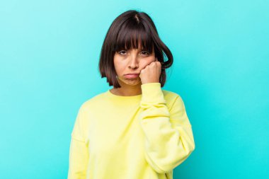 Mavi arka planda soyutlanmış, üzgün ve dalgın hisseden, kopyalama alanına bakan genç melez bir kadın..