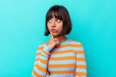 Genç melez kadın, mavi arka planda izole edilmiş. Bir strateji planlıyor, bir iş yolu düşünüyor..