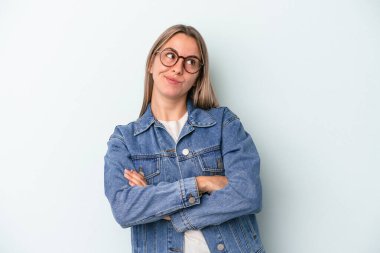 Mavi arka planda izole edilmiş genç beyaz kadın hedeflerine ve amaçlarına ulaşma hayali kuruyor.