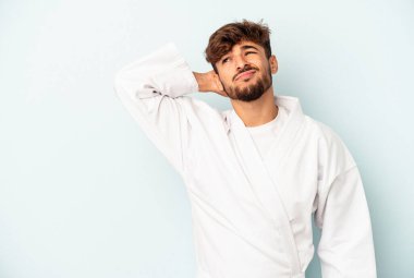 Karate yapan genç melez adam mavi arka planda izole edilmiş kafasının arkasına dokunuyor, düşünüyor ve bir seçim yapıyor..