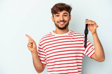 Mavi arka planda izole edilmiş bir kol saati tutan genç melez adam gülümsüyor ve boş alanda bir şey gösteriyor..