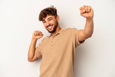 Genç melez adam gri arka planda izole edilmiş özel bir günü kutluyor, atlıyor ve enerjiyle kollarını kaldırıyor..