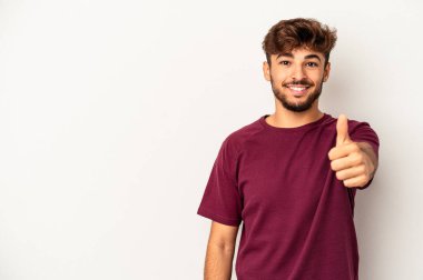 Genç melez adam gri arka planda izole edilmiş gülümsüyor ve baş parmağını kaldırıyor.