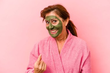 Middle age caucasian woman wearing a facial mask isolated on pink background pointing with finger at you as if inviting come closer.