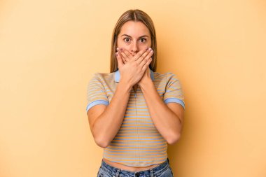 Sarı arka planda izole edilmiş genç beyaz kadın elleriyle ağzını kapatırken şok oldu..