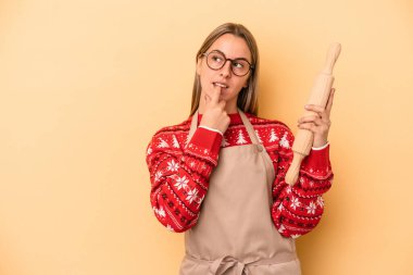 Genç fırıncı kadın Noel için kurabiye yapıyor. Sarı arka planda izole edilmiş. Bir şeyin fotokopi odasına baktığını düşünüyor..