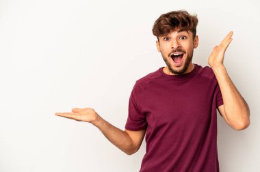 Gri arka planda izole edilmiş genç melez avuçlarında fotokopi alanı tutuyor, el üstünde tutuyor. Şaşırmış ve mutlu..