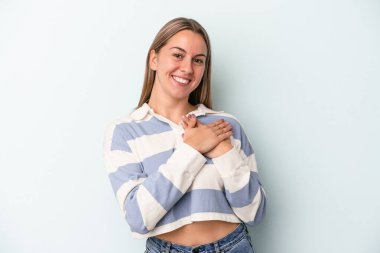 Mavi arka planda soyutlanmış genç beyaz kadın gülüyor, elini yüreğine koyuyor, mutluluk kavramını koruyor..