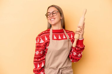 Genç fırıncı kadın Noel için kurabiye yapıyor. Sarı arka planda izole edilmiş. Gülümsüyor, neşeli ve keyifli..