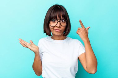 Genç melez kadın mavi arka planda izole edilmiş ve elinde bir ürün var..