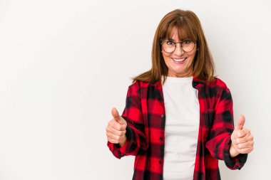 Beyaz arka planda izole edilmiş orta yaşlı beyaz kadın gülümsüyor ve başparmağını kaldırıyor.