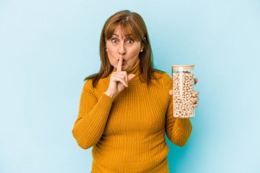 Middle age caucasian woman holding chickpea jar isolated on blue background keeping a secret or asking for silence.